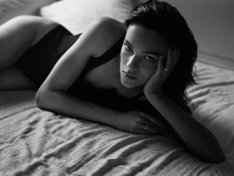 Model Lisa Louis Fratani reclining on a bed in a dark bodysuit in black and white for Vanity Fair Italia.