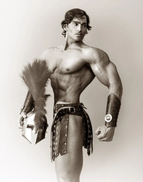 Muscular man in Roman-style armour poses indoors with a helmet and feathered plume; black and white portrait.