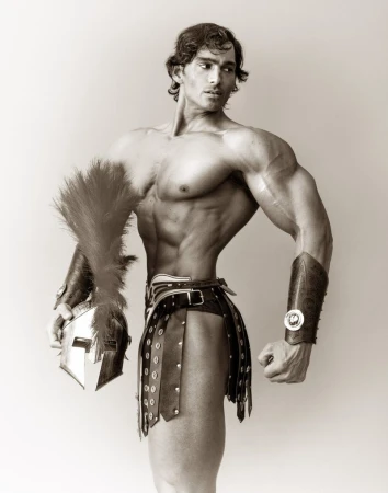 Muscular man in Roman-style armour poses indoors with a helmet and feathered plume; black and white portrait.