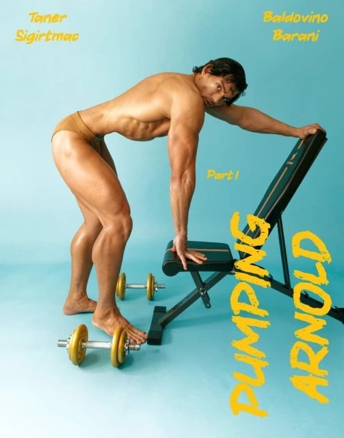 A man in tan briefs is bent over with one hand on a workout bench. The photograph is set against a light blue studio backdrop.