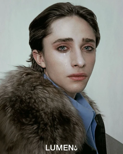 Close-up studio shot of a young adult with tear, fur-trimmed jacket, and light blue shirt against a neutral background, showcasing fashion and beauty.