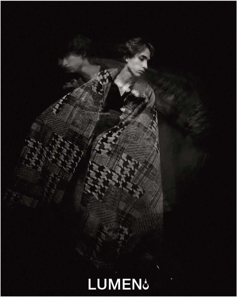 Black and white portrait of a male fashion model wrapped in a houndstooth-patterned blanket, creating an artistic double exposure effect.