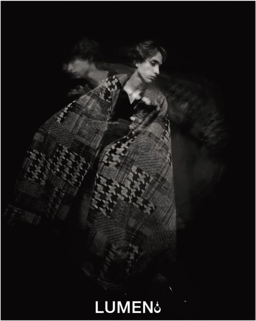 Black and white portrait of a male fashion model wrapped in a houndstooth-patterned blanket, creating an artistic double exposure effect.