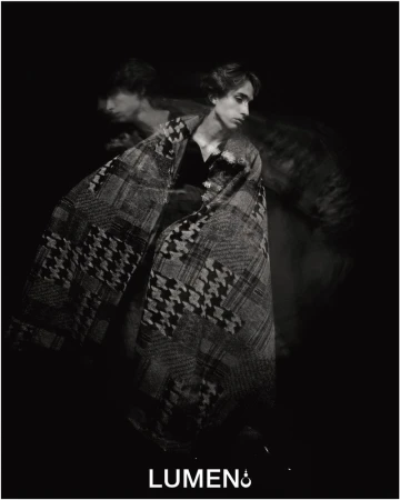 Black and white portrait of a male fashion model wrapped in a houndstooth-patterned blanket, creating an artistic double exposure effect.