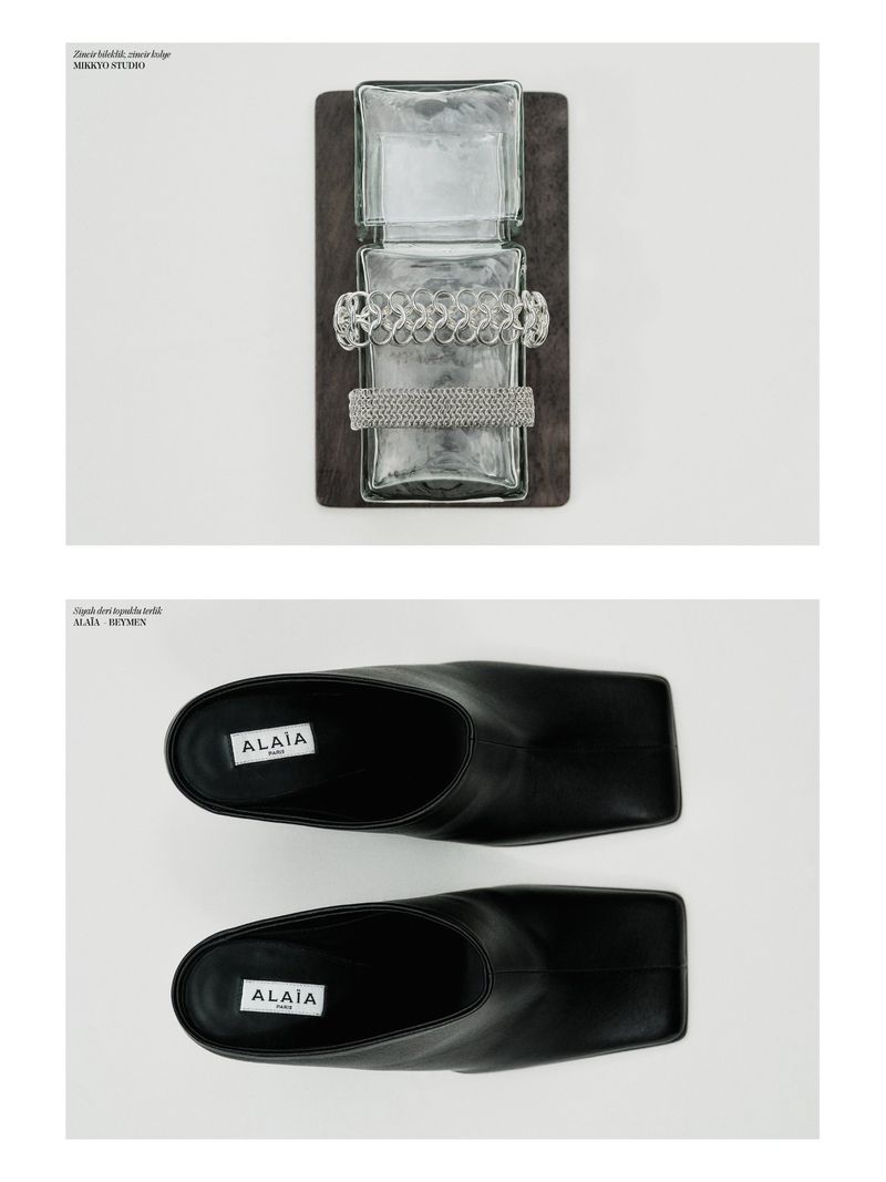 Still life editorial shot of a glass display holding jewellery and a pair of black Alaïa mules, captured in a bright, neutral studio.