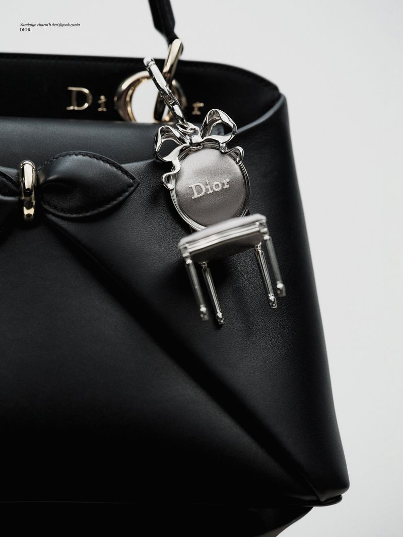 Close-up studio shot of a black Dior handbag with silver hardware and a chair-shaped charm. Fashion, product photography, luxury.