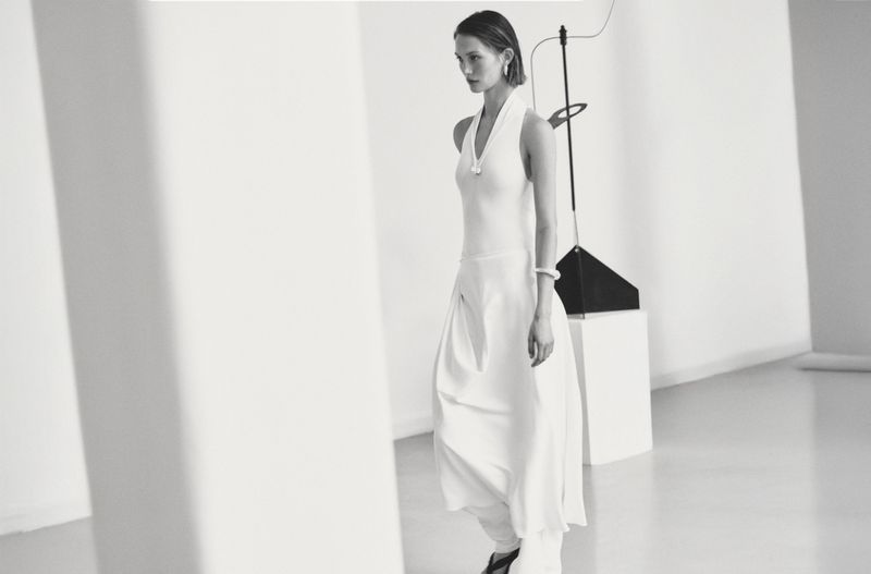 Elegant adult woman in white dress posing in a light, modern studio. Minimalist fashion photography for apparel and style.