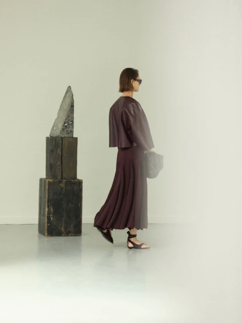 A stylish adult female in a plum-colored ensemble poses in a minimalist studio with modern art; clean lines and soft lighting.
