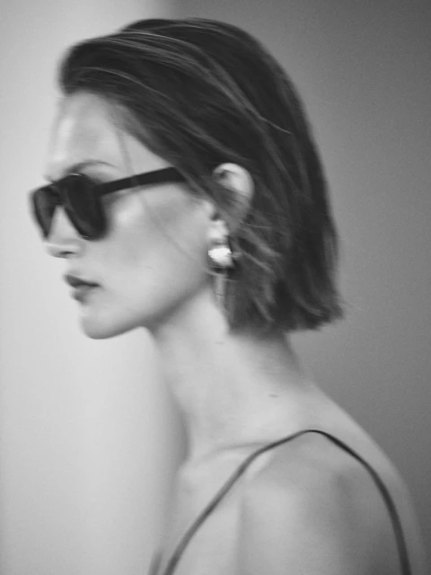 Portrait of a young woman with bob haircut wearing sunglasses and large earrings in a black-and-white fashion editorial photograph.