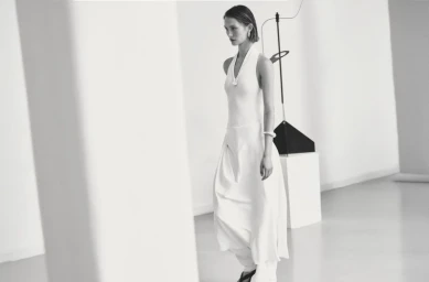 Model in a white halter dress walking in a modern minimalist interior for Massimo Dutti Studio June'25 campaign.