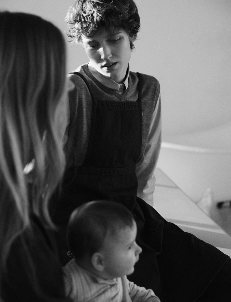 Pauline Schubach seated in a pinafore dress looking down towards a baby in a black and white editorial by Stefano Galuzzi.