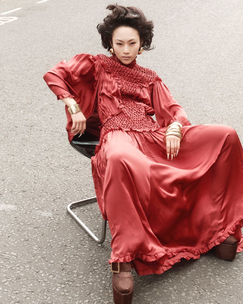 Elegant Asian woman in a red dress sitting on a chair outdoors. Fashion editorial photography with focus on model and clothing details.