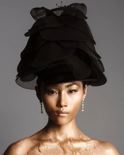 Portrait of an Asian woman with gold body paint and an elaborate black headpiece on a gray background. Beauty and fashion concept.