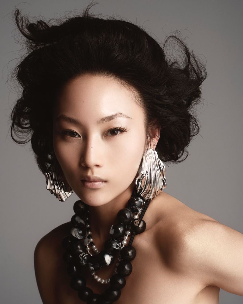 Model Wawa Li wearing statement silver fluted earrings and a chunky black beaded necklace against a seamless grey backdrop.