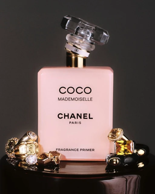 Still life studio shot of Coco Mademoiselle Fragrance Primer by Chanel, displayed with gold rings on a reflective black surface.