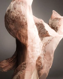 Billowing sheer blush pink fabric with ornate brown patterns floating in mid-air against a neutral studio backdrop.