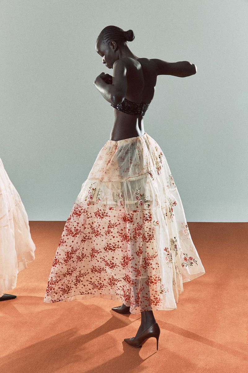 Fashion shot of African American woman in floral dress posing with arms up in a studio with a light background and terracotta floor.