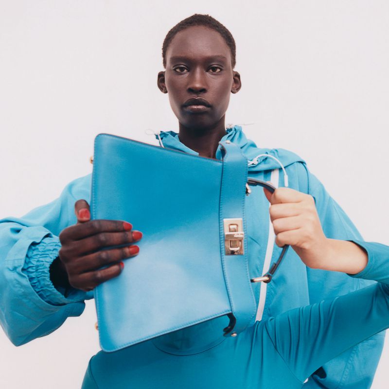 Close-up of an adult woman holding a bright blue leather handbag in a white photo studio with natural light and a minimalist aesthetic.
