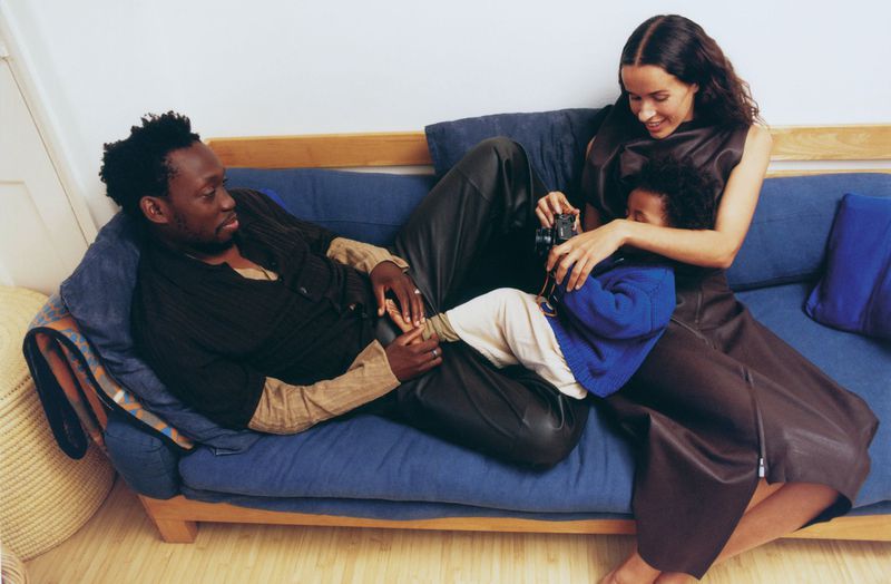A relaxed family moment on a blue couch: a man, a woman, and a child with a camera create a candid lifestyle scene in a home interior.