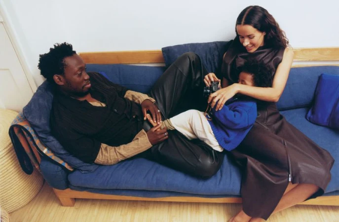 A relaxed family moment on a blue couch: a man, a woman, and a child with a camera create a candid lifestyle scene in a home interior.