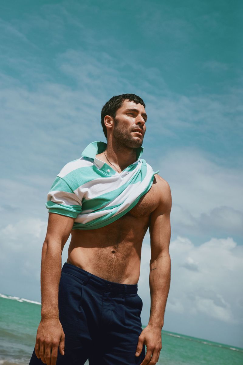 Man wearing a striped polo shirt pulling it off against a bright sky and coastal background