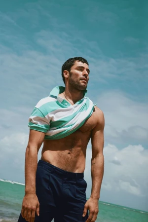 Man wearing a striped polo shirt pulling it off against a bright sky and coastal background