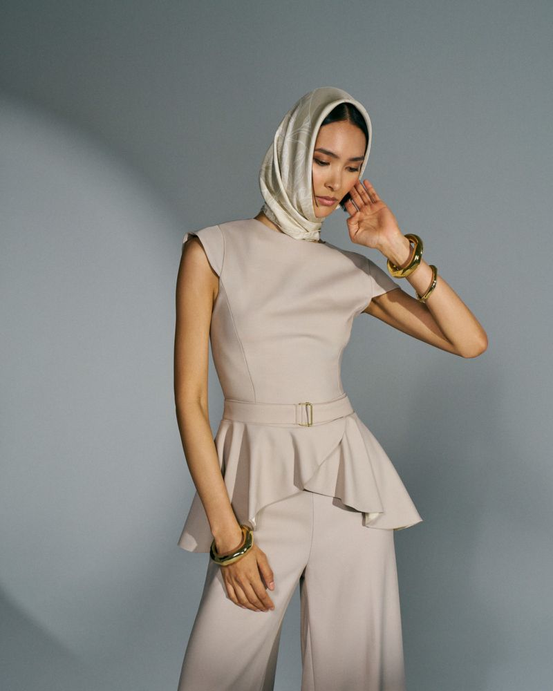 Elegant woman in a headscarf and matching two-piece outfit, posing against a soft gray backdrop with subtle studio lighting.