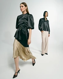 Two fashion models posing in satin blouses, a gold midi skirt, and wide-leg trousers against a white studio background.