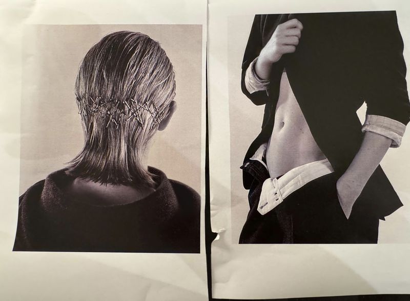 Black-and-white studio fashion shot showcases a person's back with hair secured by safety pins and another person's midsection in a blazer.