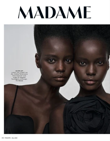 Close-up magazine cover featuring two dark-skinned adult females in elegant black attire against a neutral backdrop, capturing a high-fashion aesthetic.