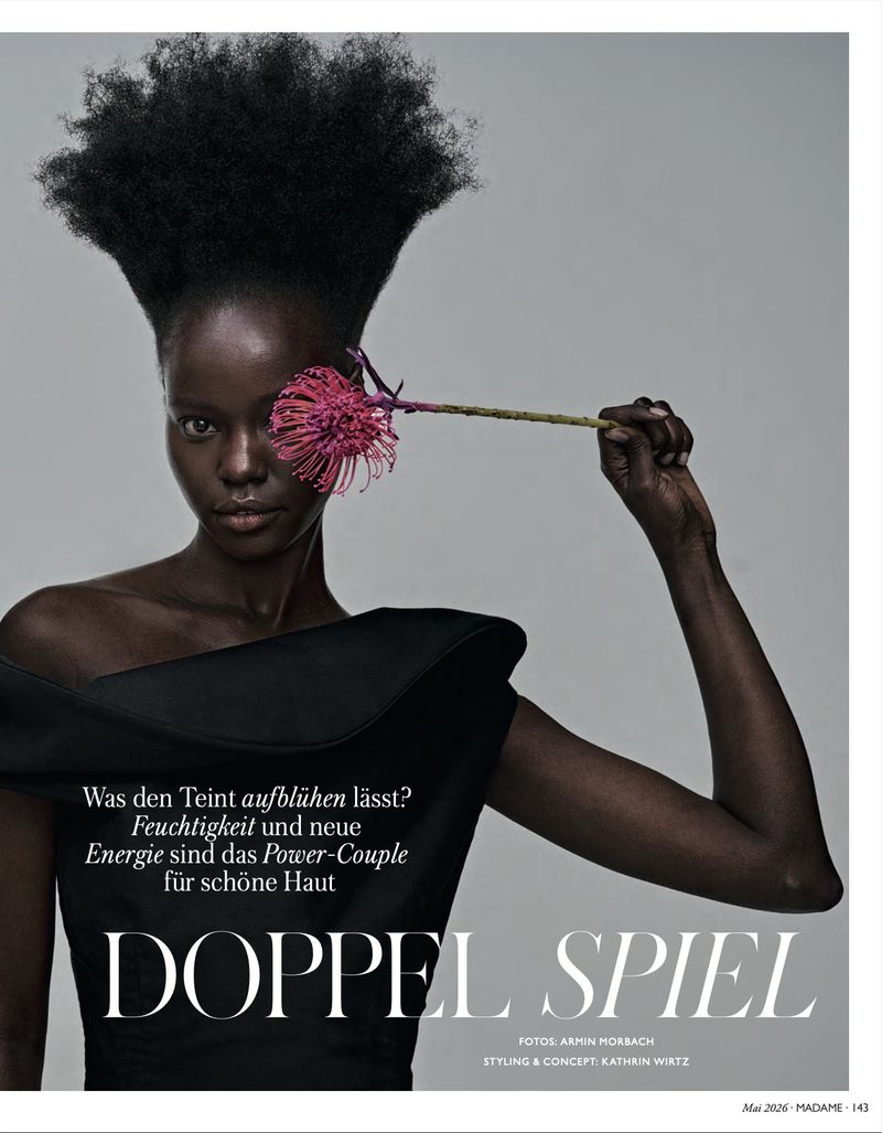 Black female model wearing black couture fashion with tall afro and holding flower to her eye in a studio beauty shot.