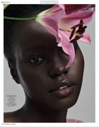 Close-up beauty portrait of a Black woman with radiant skin posed beside a large pink lily flower.