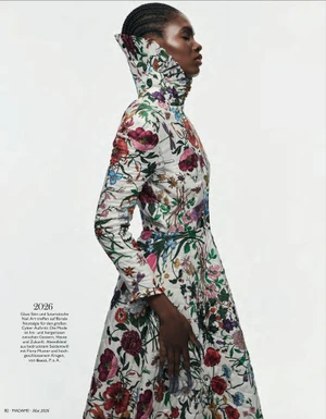 Ayobami Okekunle in profile wearing a high-collared floral print coat dress against a white studio background.