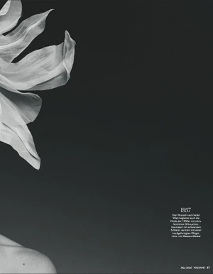 Monochrome close-up of a sculptural white floral fascinator and bare shoulder against a dark negative space background.