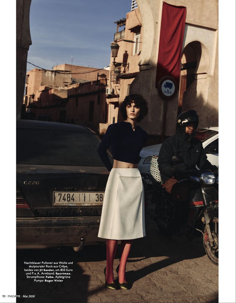 Fashion shot in Morocco featuring a woman in a navy top and white skirt, with a man on a motorcycle in the background.