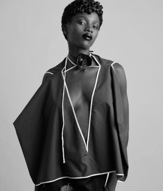 Monochrome fashion portrait of a young Black woman with short curly hair wearing a dark top with white trim and a statement necklace.