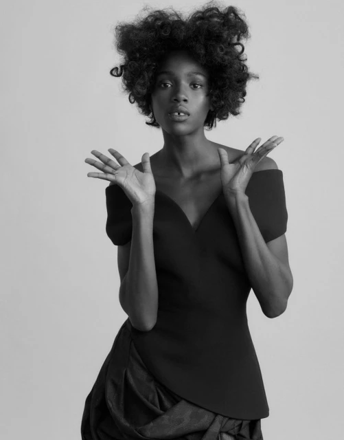 Black and white portrait of an African American woman with dark curly hair in a dress, posing with her hands up and a neutral expression.