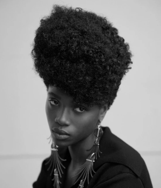 Close-up portrait of a stylish Black woman with afro and dangling earrings against a plain white backdrop in monochrome.