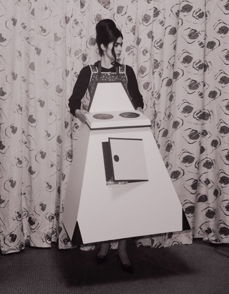 Woman in stove costume standing against patterned backdrop. Black and white photograph of retro fashion and creative portrait.