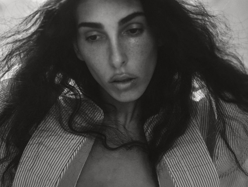 Striking black and white portrait of a woman with long dark hair wearing a striped shirt, captured in soft, natural light.