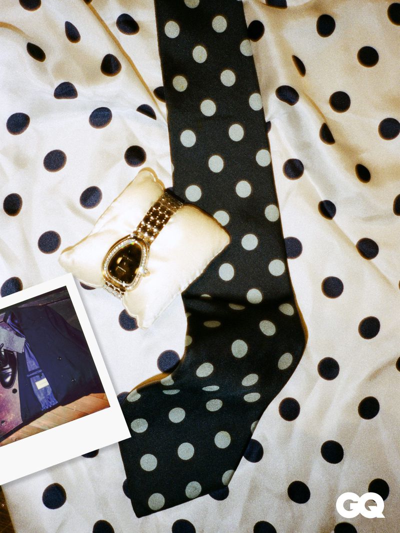 Flat lay of gold watch on a pillow, tie, instant photograph, and polka dot fabric. GQ Magazine logo visible in the corner.