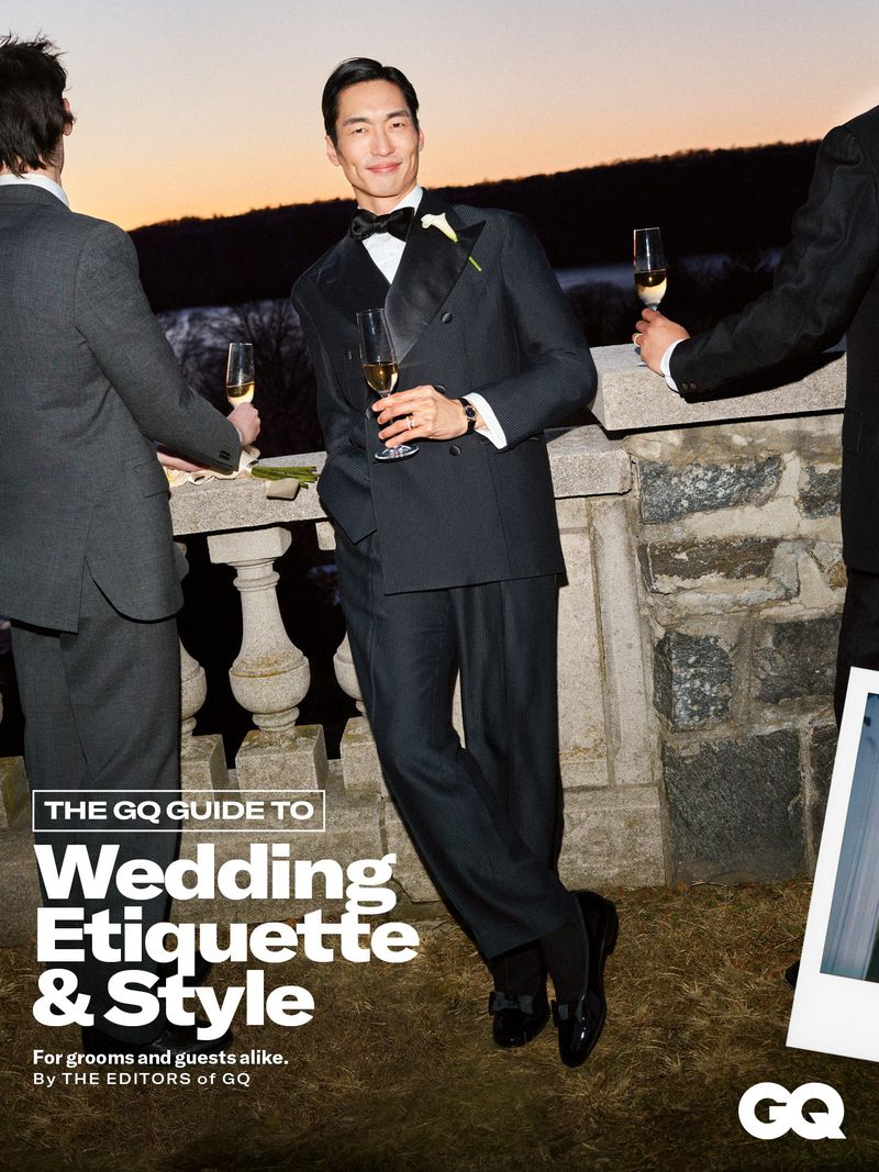 Well-dressed man in tuxedo holds champagne outdoors, with two men in suits nearby on balcony. Evening light and GQ magazine cover visible.