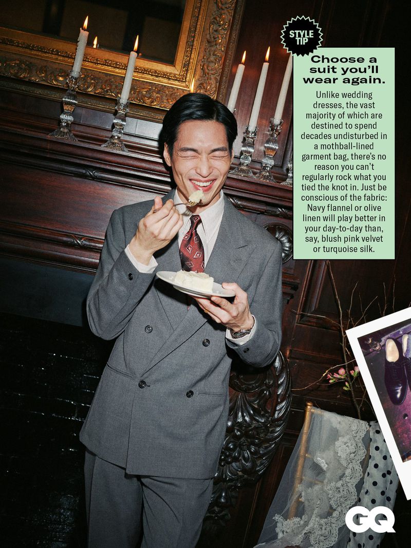 Adult Asian male in a gray suit enjoys cake indoors, near an ornate fireplace and candelabras. GQ logo visible in lower right corner.