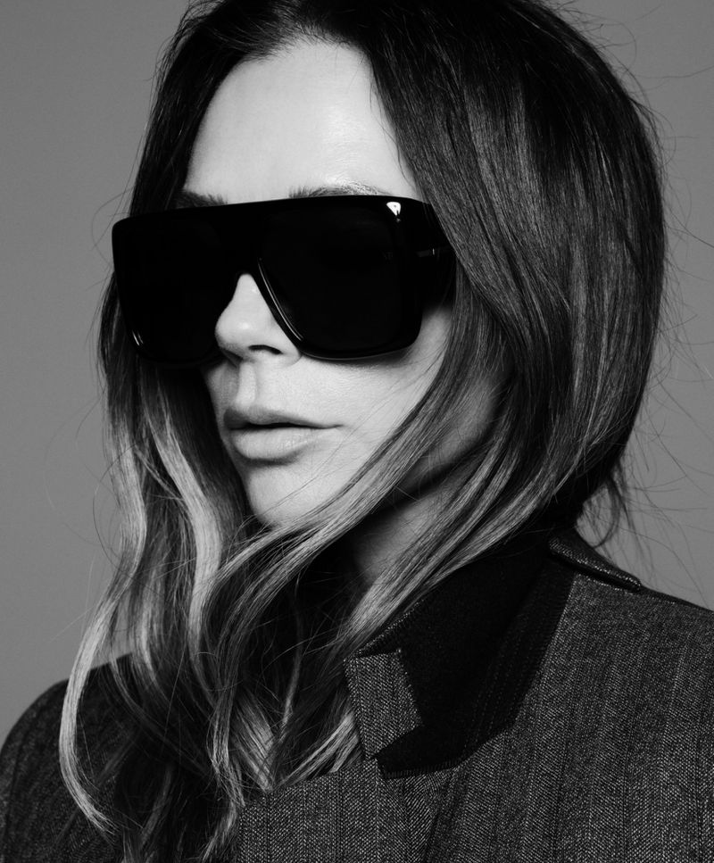 Monochrome portrait of a woman with shoulder-length hair, wearing oversized black sunglasses and a dark grey wool coat, set against a grey background.