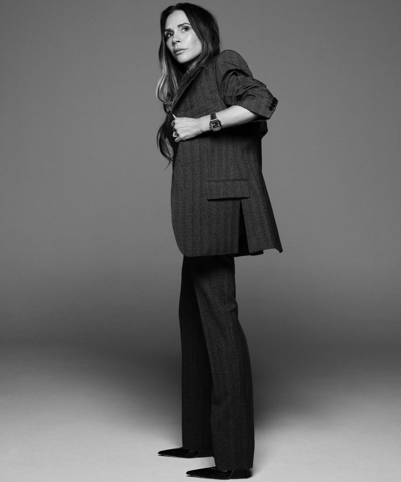 Black and white portrait of a stylish adult woman in a herringbone blazer and trousers, accented with a watch and black pointed shoes.