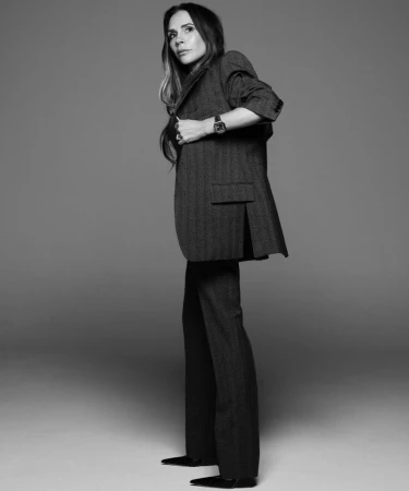 Black and white portrait of a stylish adult woman in a herringbone blazer and trousers, accented with a watch and black pointed shoes.