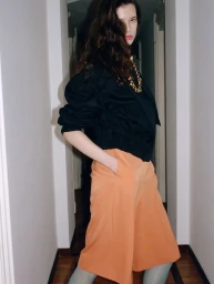 Model Sandra Murray posing in a black puff-sleeve top and peach culottes in an interior hallway for D Repubblica.