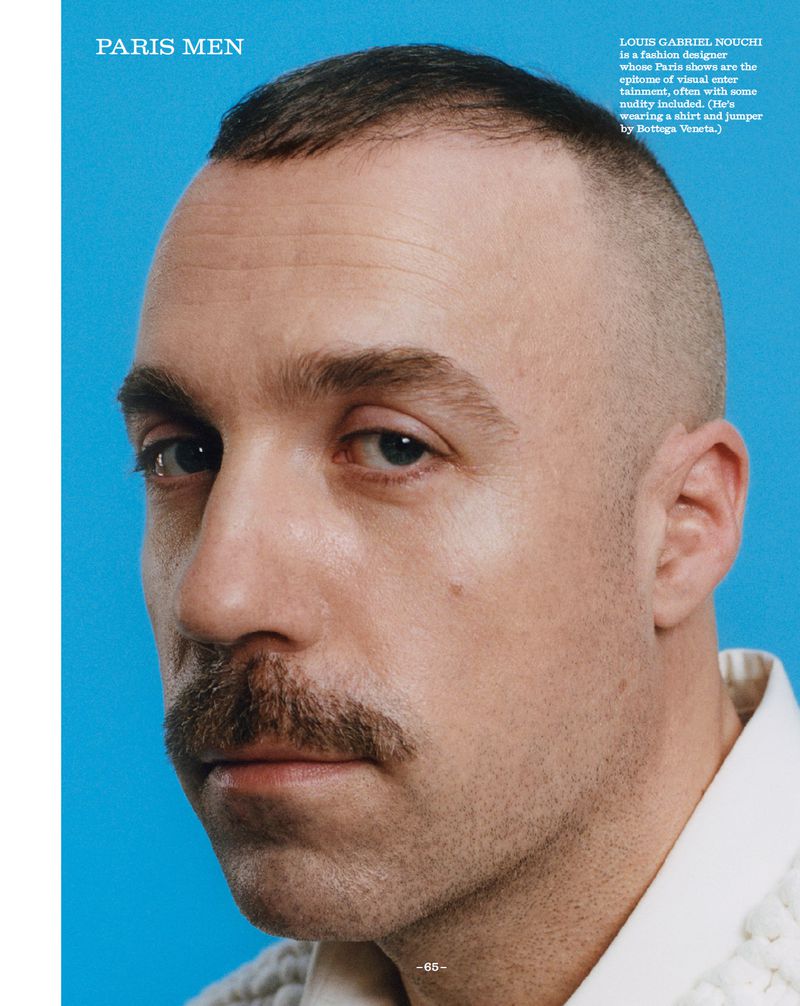 Close-up portrait of a man with a mustache against a solid blue backdrop, featuring a short haircut and a neutral expression.