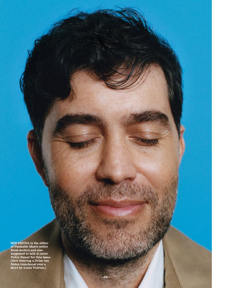 Portrait of a man with dark hair, closed eyes, and light stubble, wearing a tan jacket against a bright cyan background in a close-up shot.