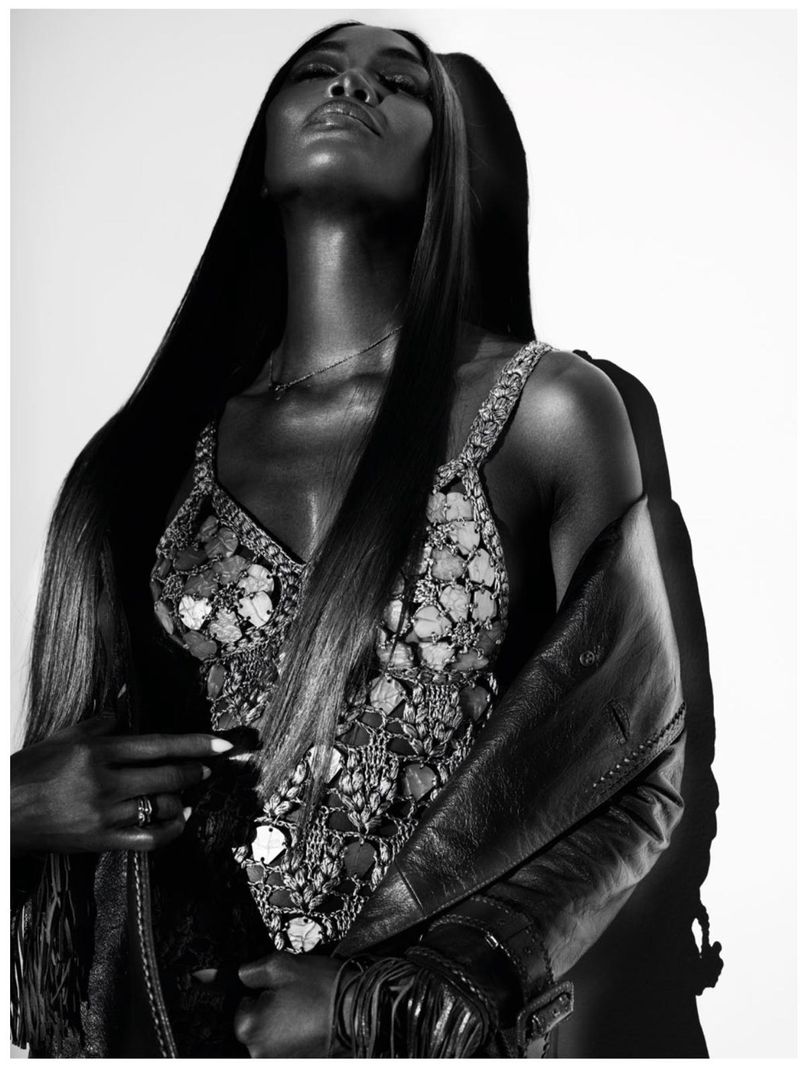 Black and white studio shot of a striking adult female fashion model with long dark hair, wearing an embellished top and leather jacket.